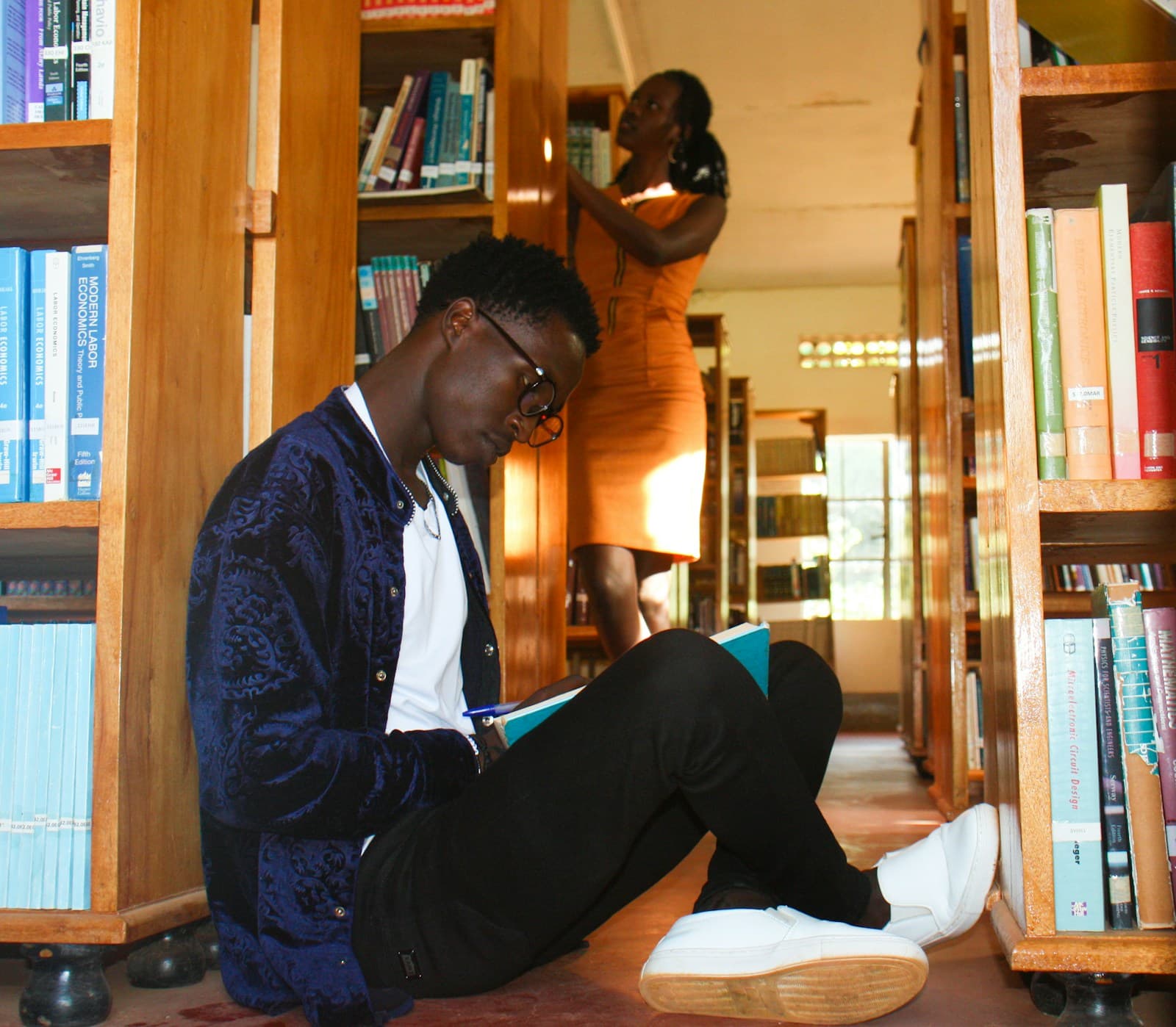 A man reading a book while seated between library shelves